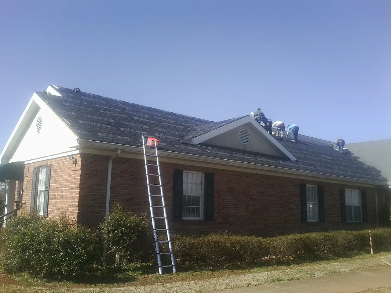 Crew tearing shingles off a brick ranch roof with a ladder set — Emergency Roof Repair work by our crew in Donnelsville