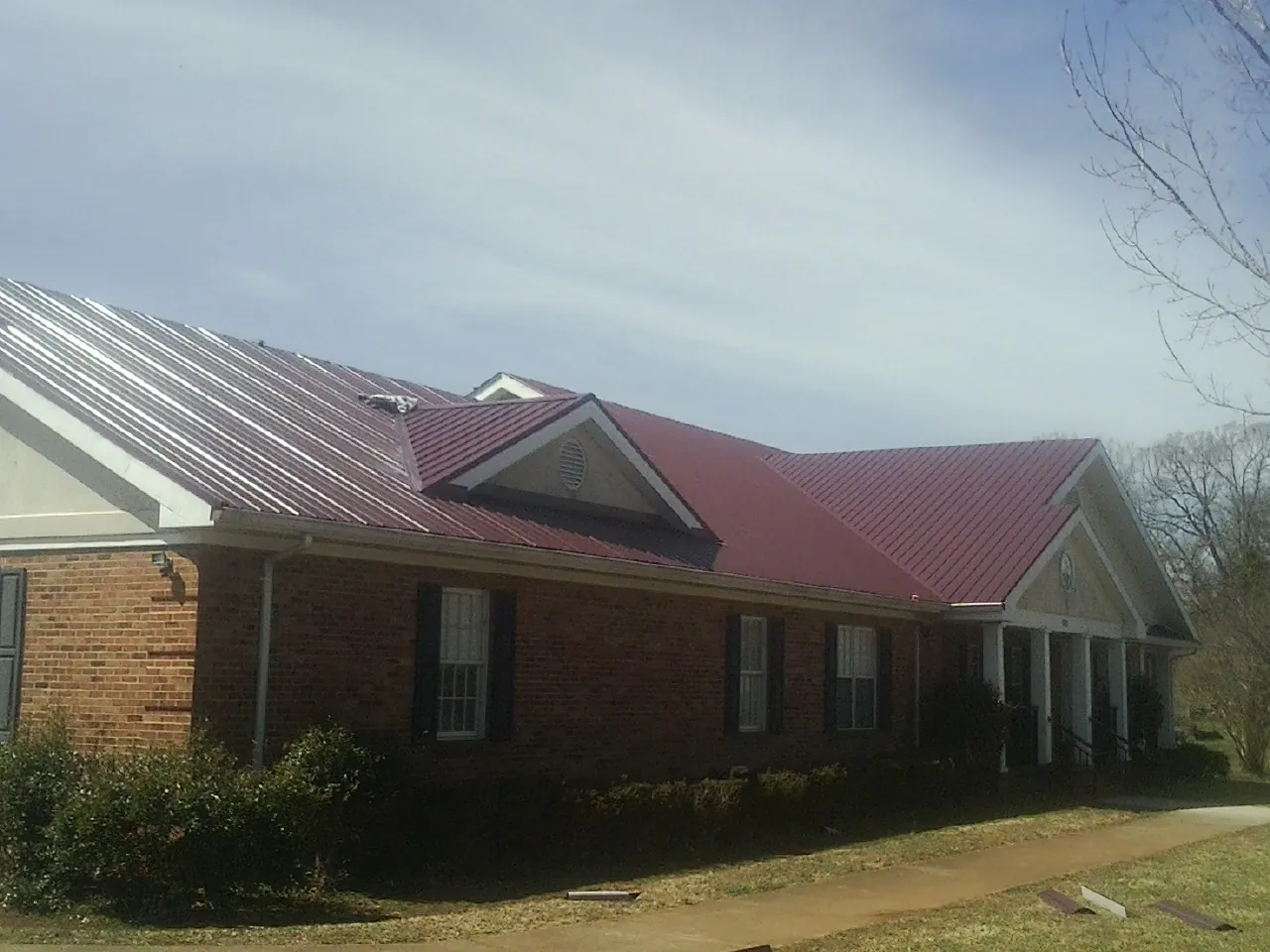 Red metal roof with gabled entries on a long brick building, from a Hail Damage Roof Repair job in Donnelsville