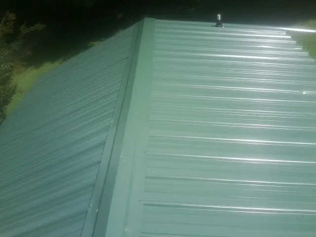 New green metal panels meeting at the ridge of a roof — Flat Roof Repair work by our crew in Donnelsville