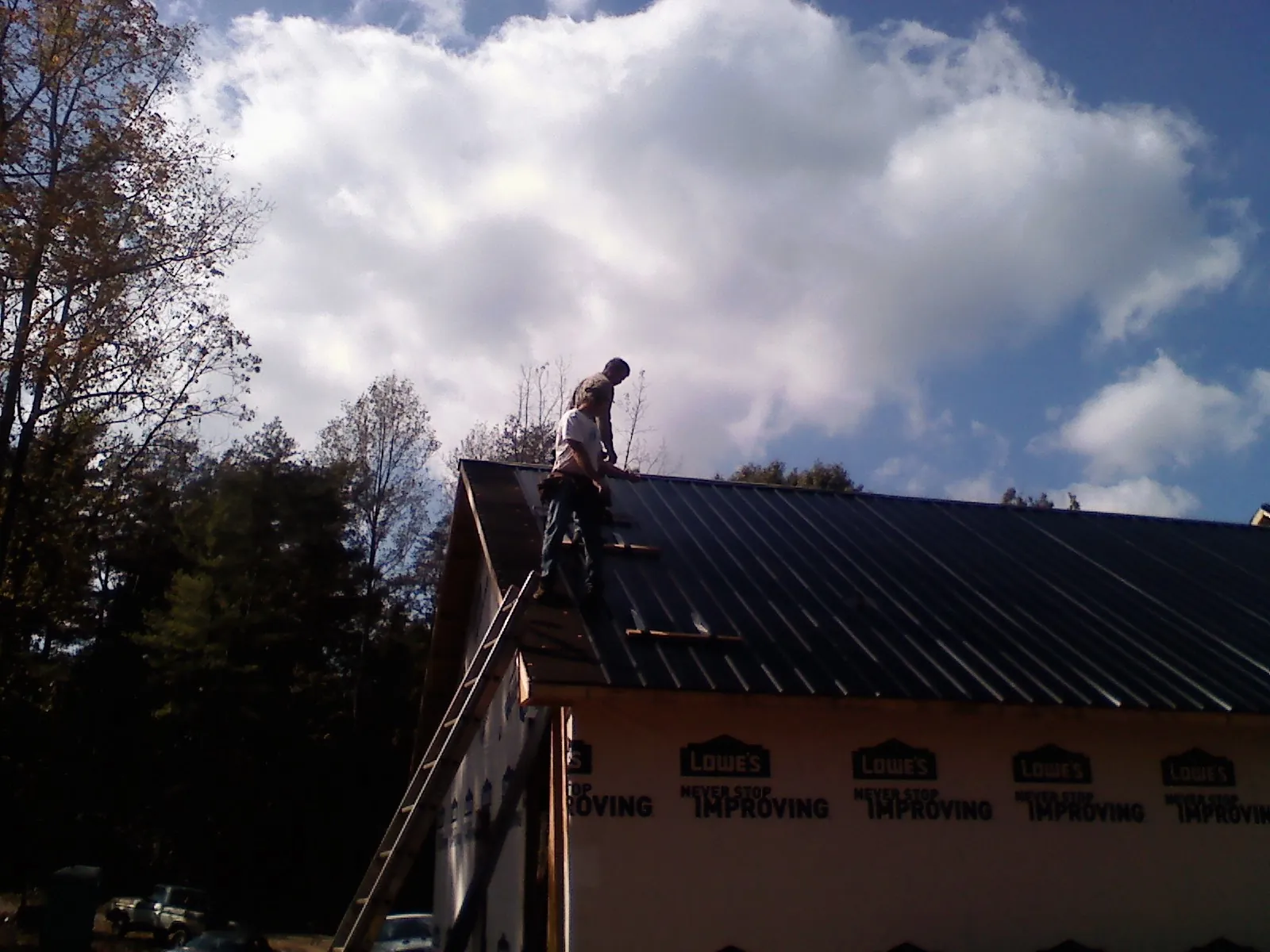 Roofer fastening dark metal panels high against a cloudy sky, from a Roof Inspection job in Donnelsville