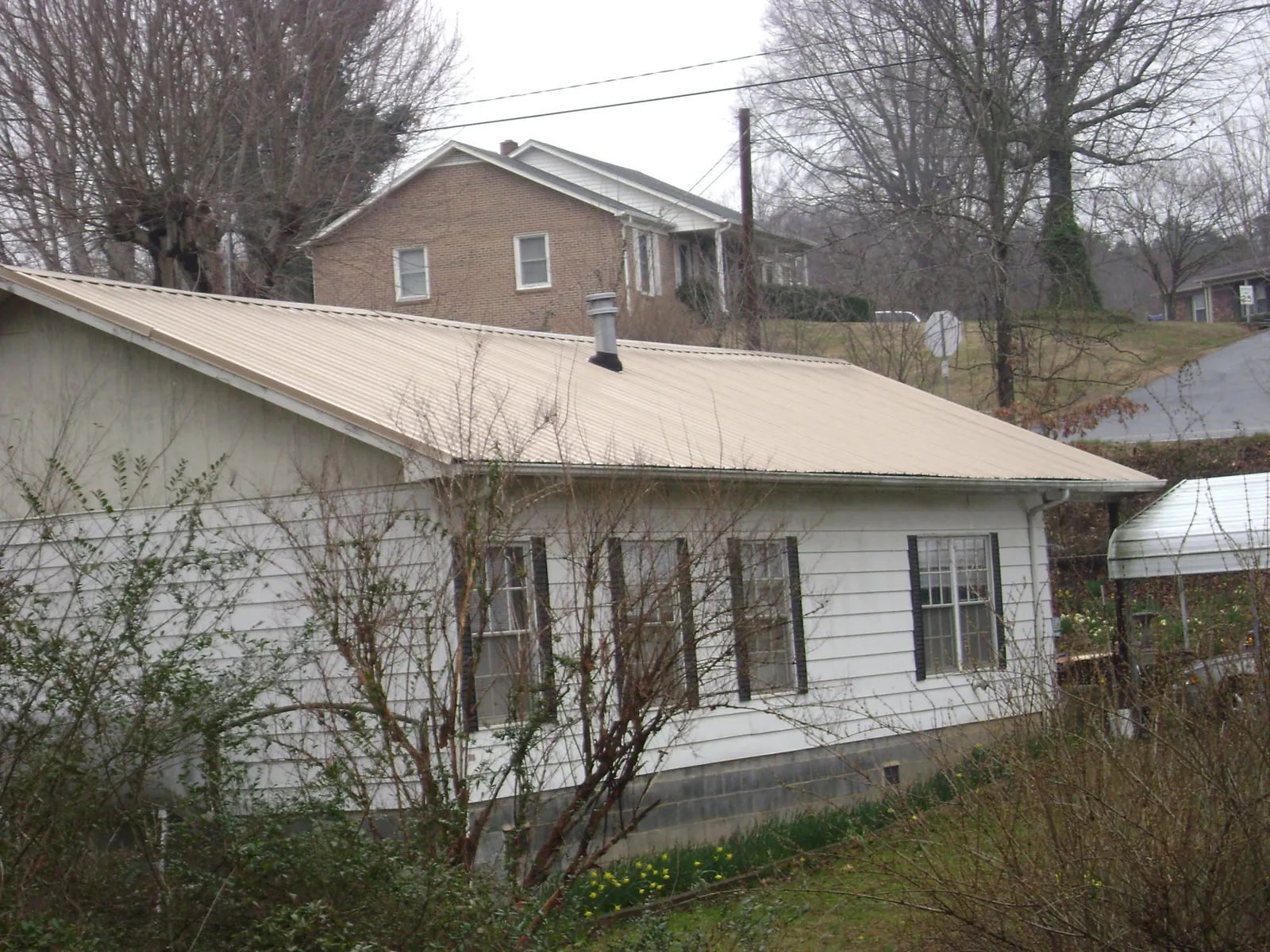 Tan metal roof on a white sided house set into a hillside — Commercial Roofing by Roofing Brothers in Donnelsville