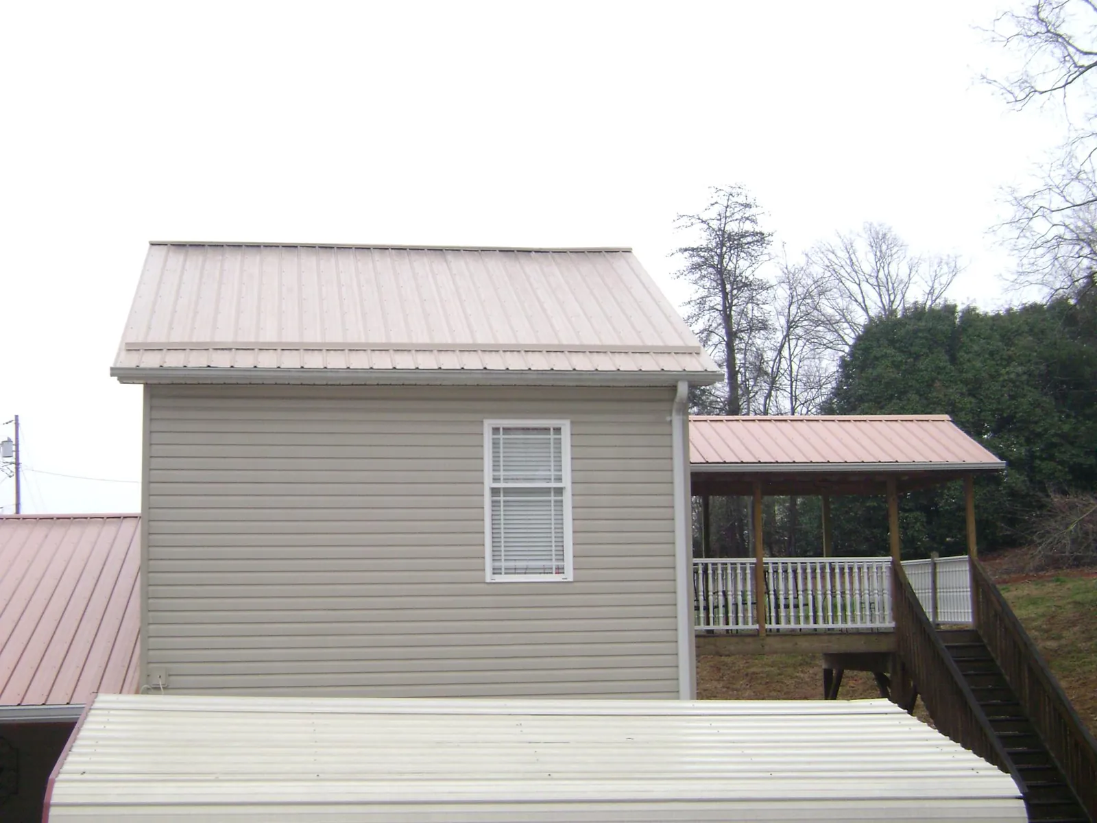 Tan metal roofs on a two story addition and attached porch, from a Roof Replacement job in Donnelsville